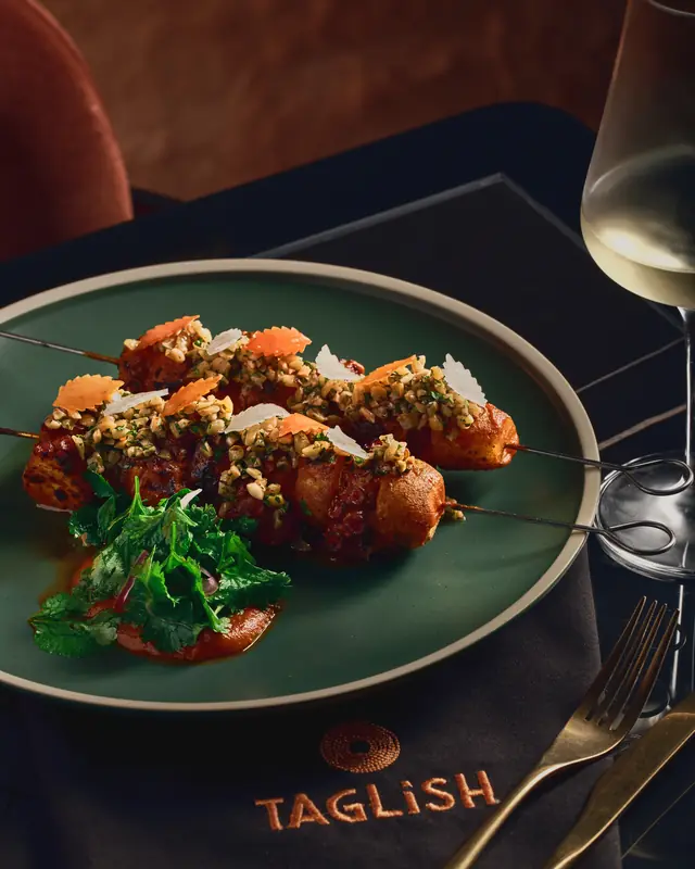 Grilled octopus skewer on a green plate with herbs and pili gremolata